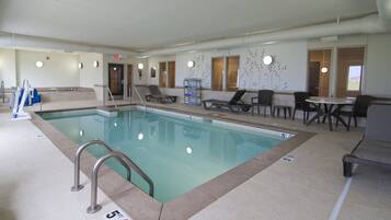 A swimming pool with a 5 ft depth marker, lounge chairs, and a seating area with tables.