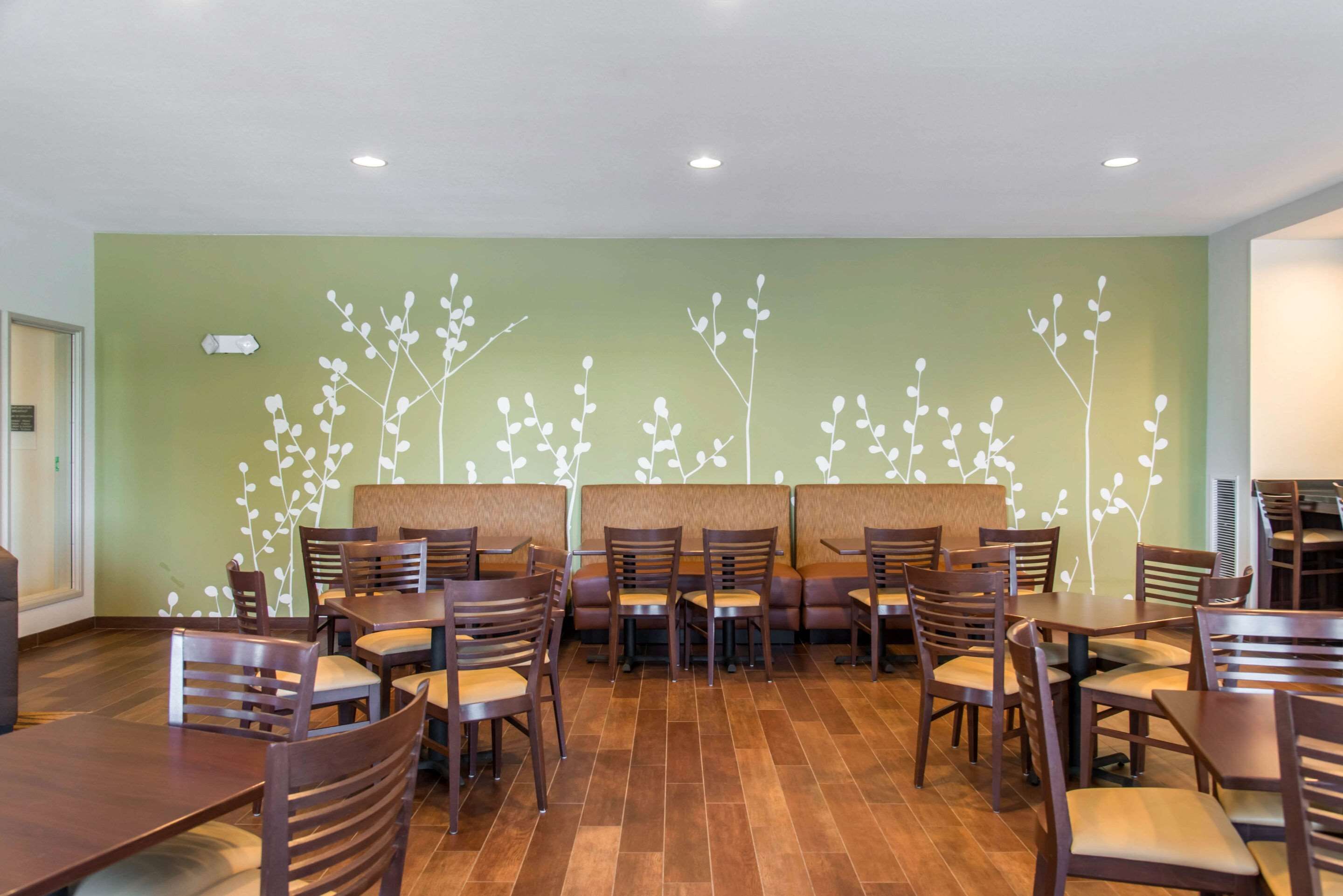 A restaurant with booths and tables, a green wall with a white branch pattern, and wooden flooring.