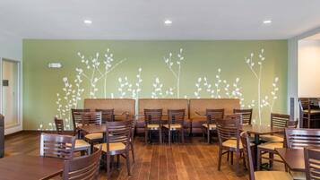 A restaurant with booths and tables, a green wall with a white branch pattern, and wooden flooring.