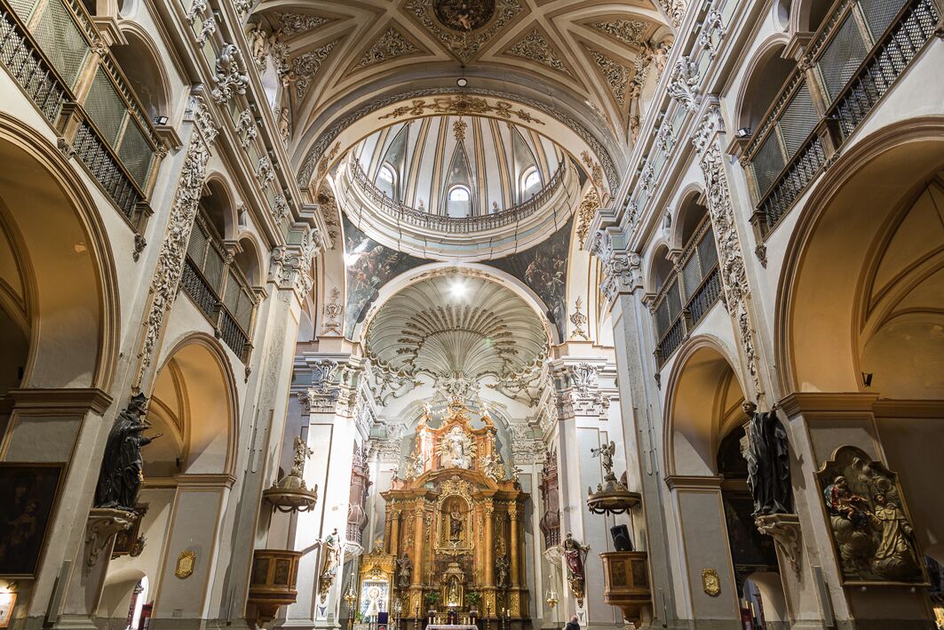 L’intérieur d’une église richement décorée, avec de hauts plafonds, des fresques détaillées et un autel central.