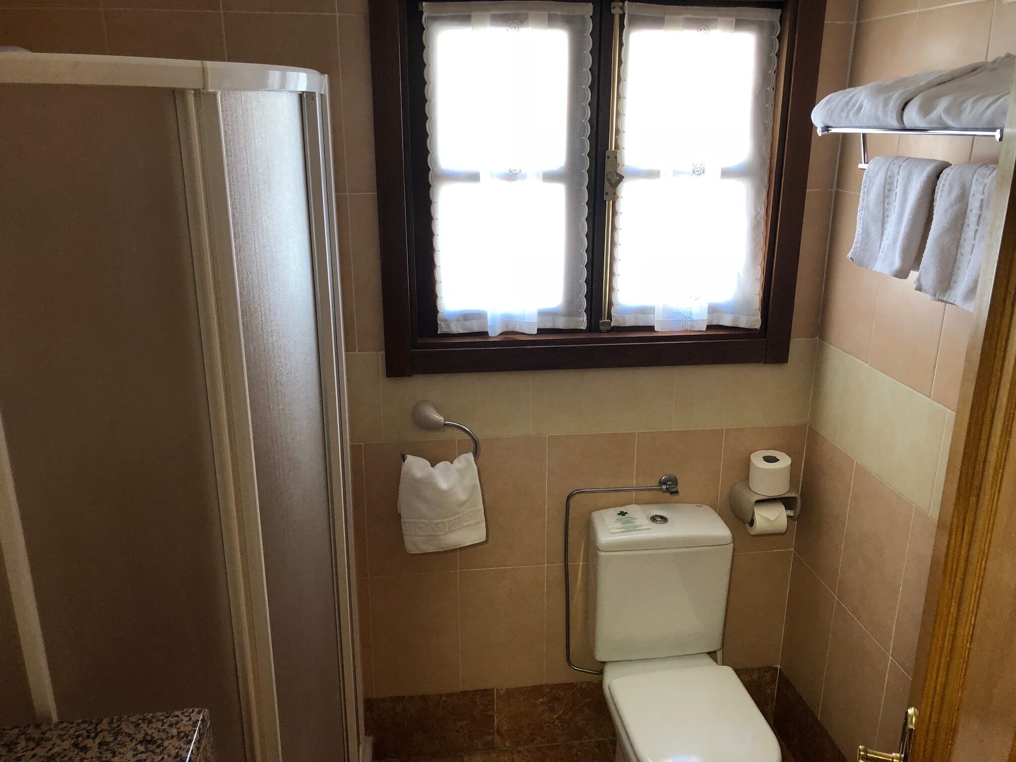 A small bathroom with a toilet, a towel rack, and a window with curtains.