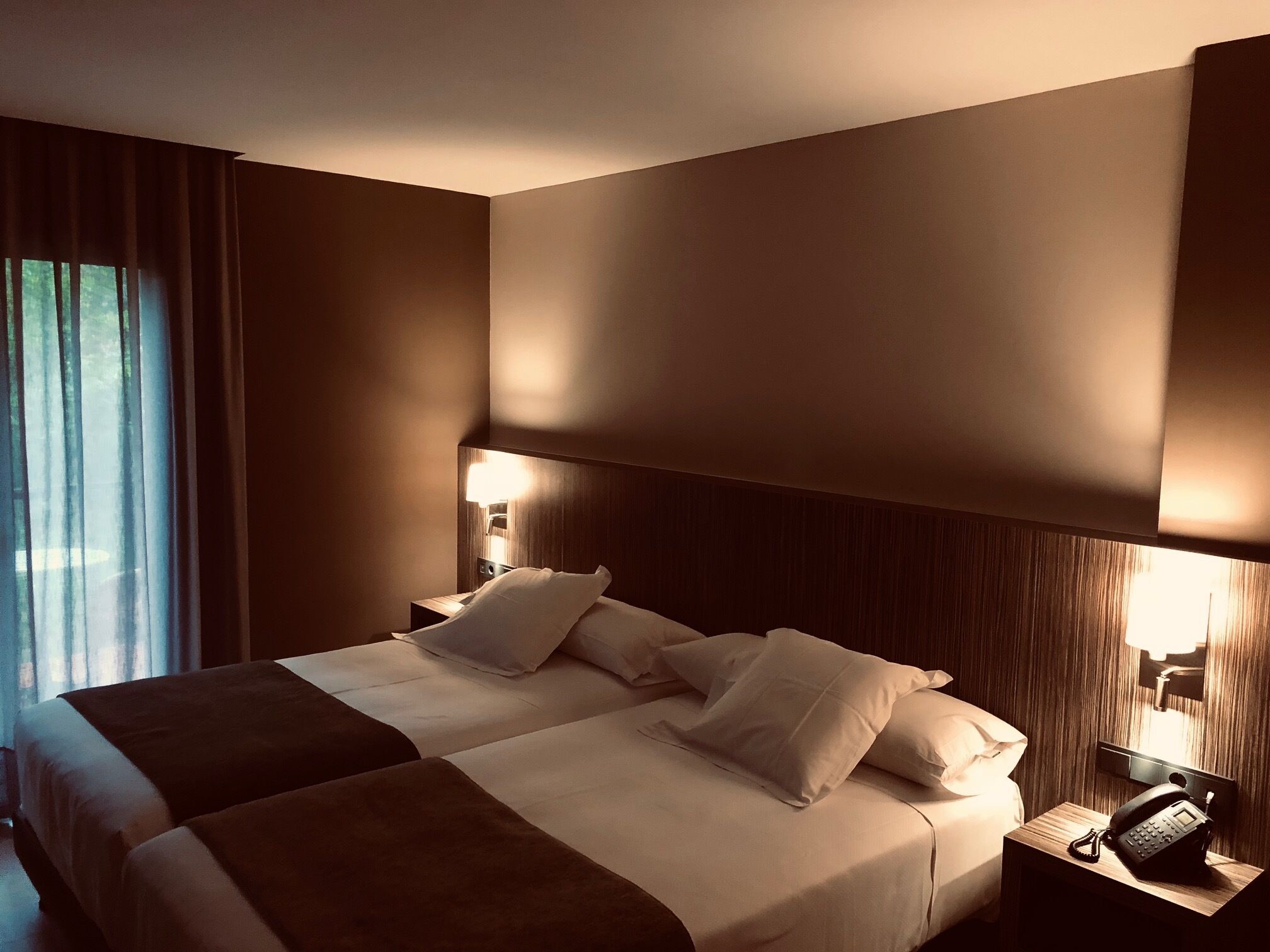 Una habitación de hotel con una cama grande, dos mesitas de noche, un teléfono y una ventana con cortinas.