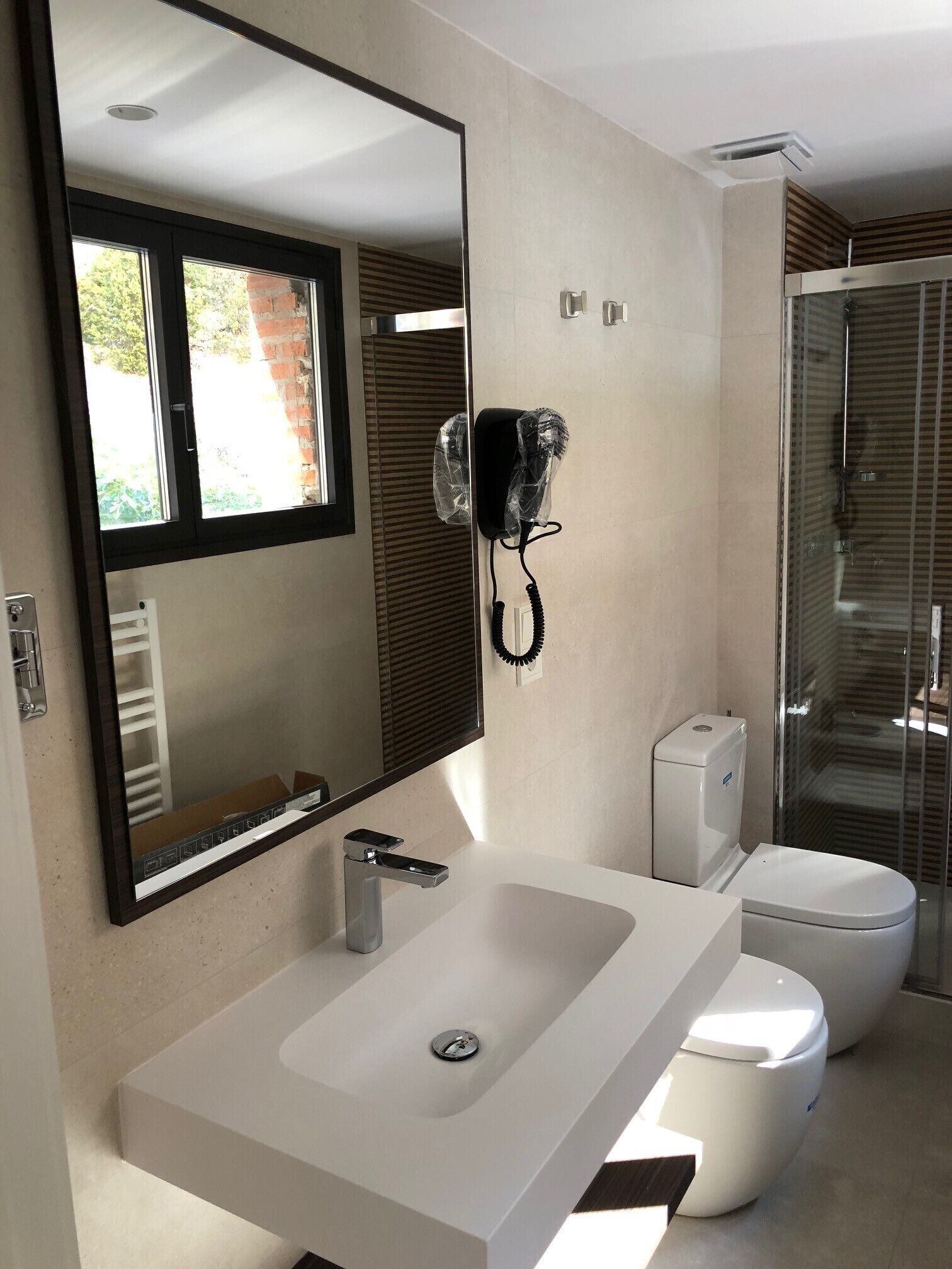 A modern bathroom with a large mirror, a white sink, a toilet, and a shower area.