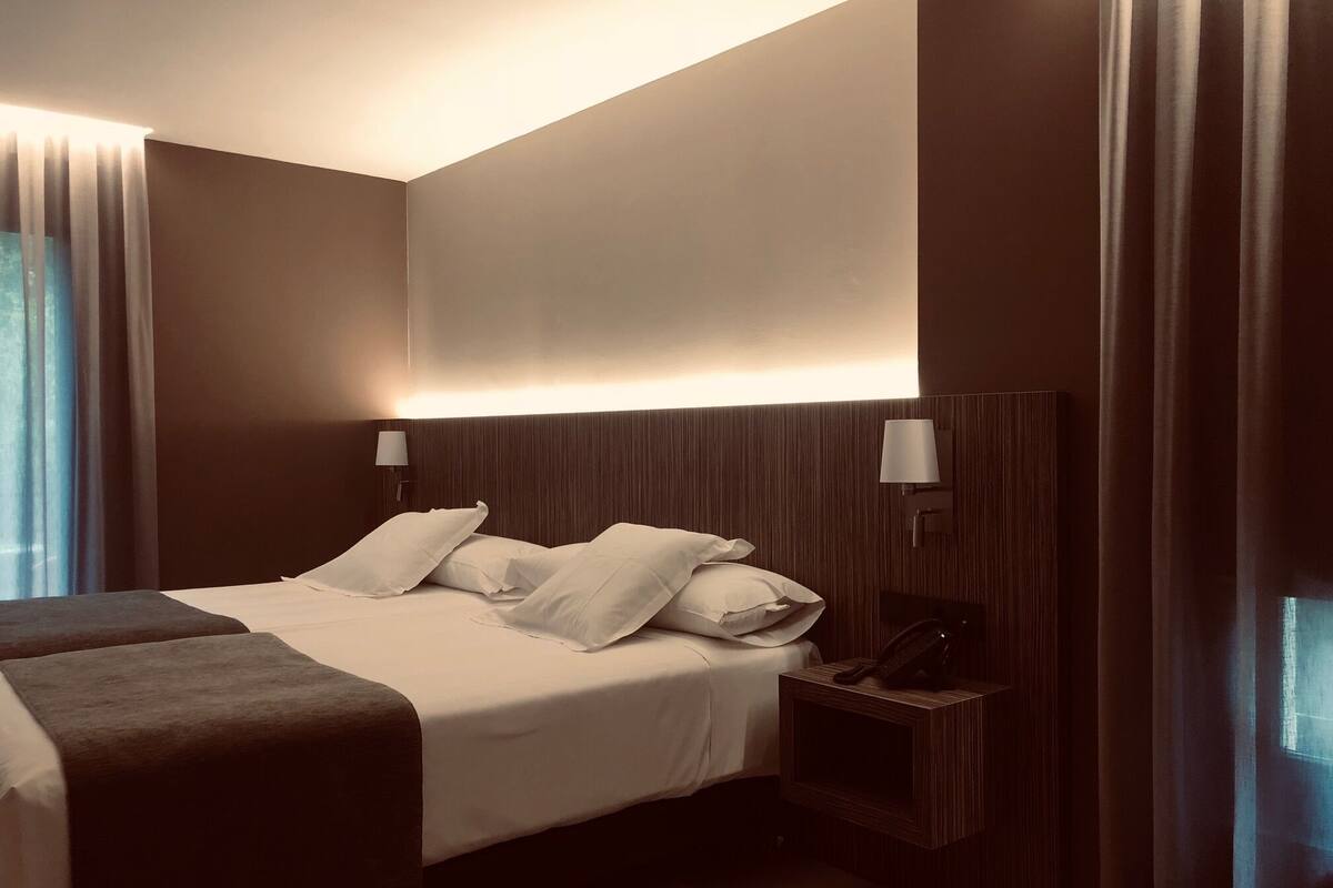 Una habitación de hotel moderna con una cama grande, dos mesitas de noche y un cabecero con iluminación integrada.
