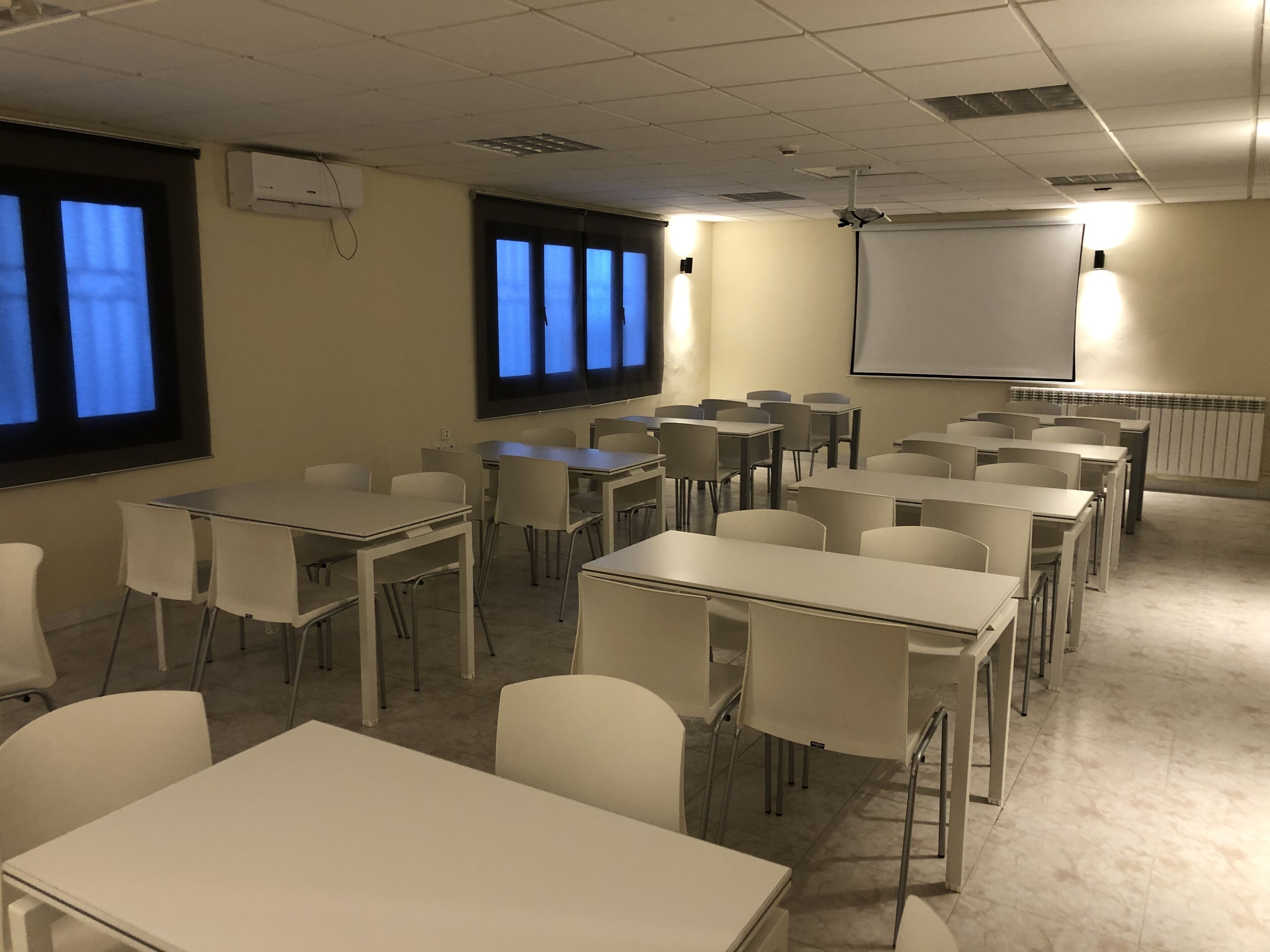 A classroom with white tables and chairs, a projector screen, and a whiteboard.