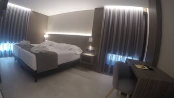 A hotel room with a bed, bedside table, lamp, chair, and desk.