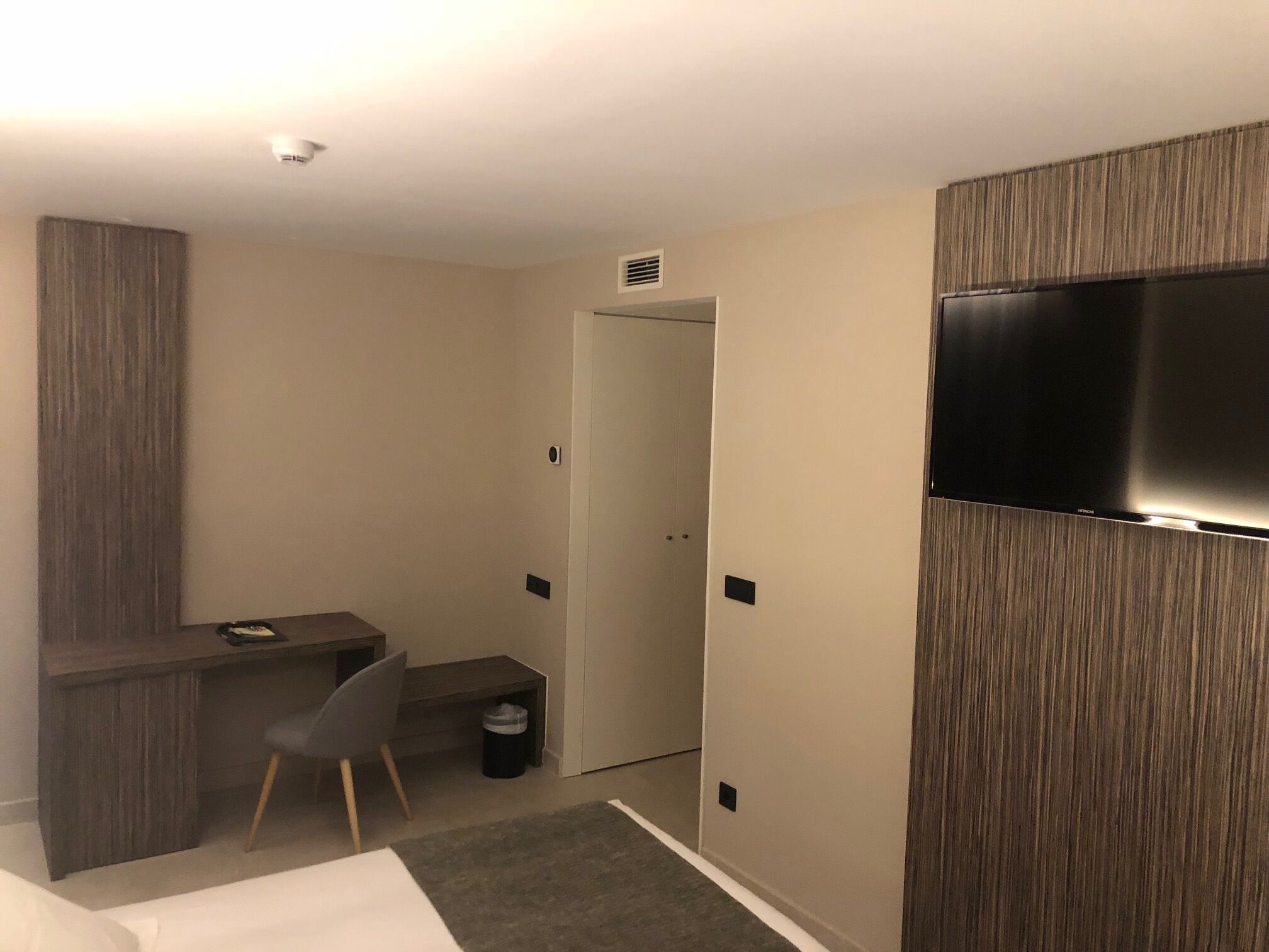A hotel room with a bed, a desk, a chair, a TV, and a wardrobe.