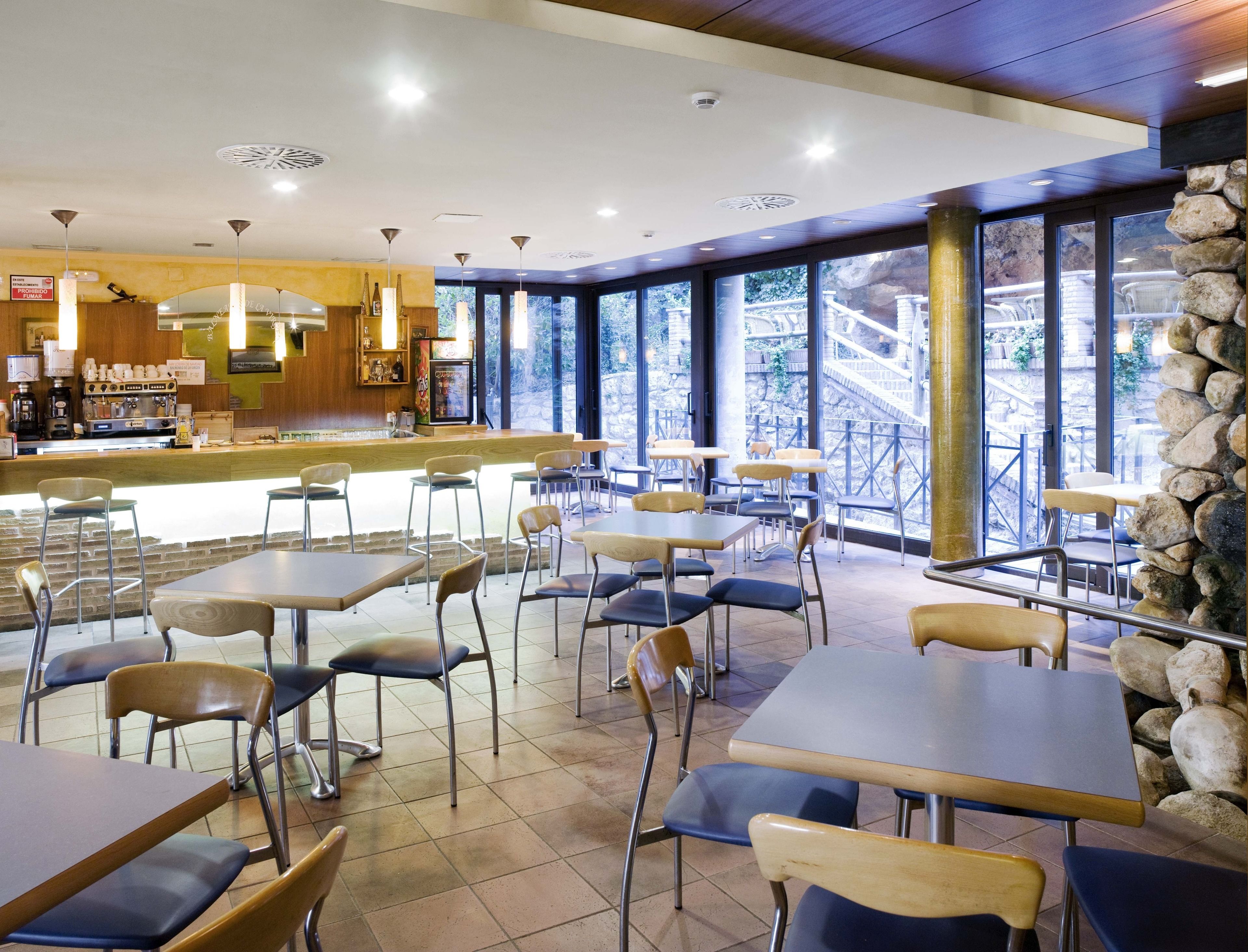 A restaurant with a bar area, tables, chairs, and large windows offering a view of a bridge and greenery.