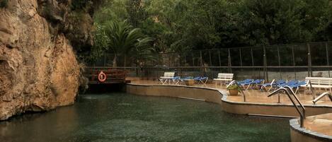 A swimming pool with clear water, surrounded by rocky cliffs and greenery.