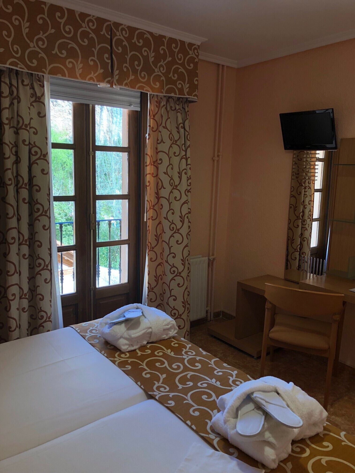 A hotel room with two beds, a desk, a chair, a TV, and a window with curtains.