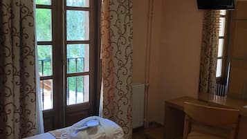 A hotel room with two beds, a desk, a chair, a TV, and a window with curtains.