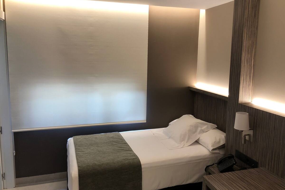 Una habitación de hotel con una cama, una mesita de noche con lámpara y un teléfono en la pared.