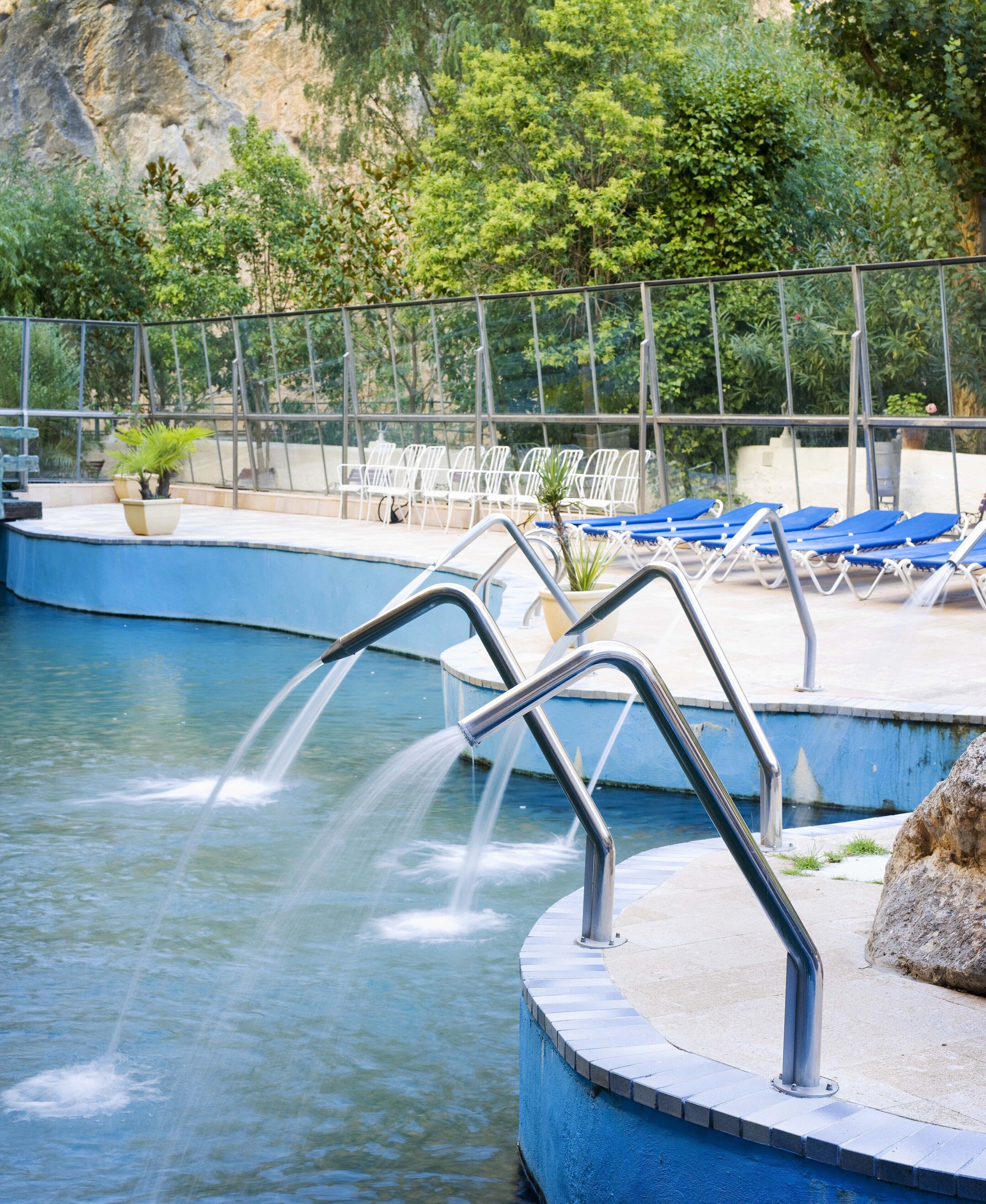 A pool area with multiple water jets, lounge chairs, and potted plants.