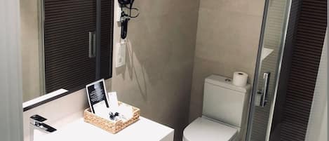 Un baño moderno con tocador blanco, secador de pelo, inodoro y cabina de ducha de vidrio.