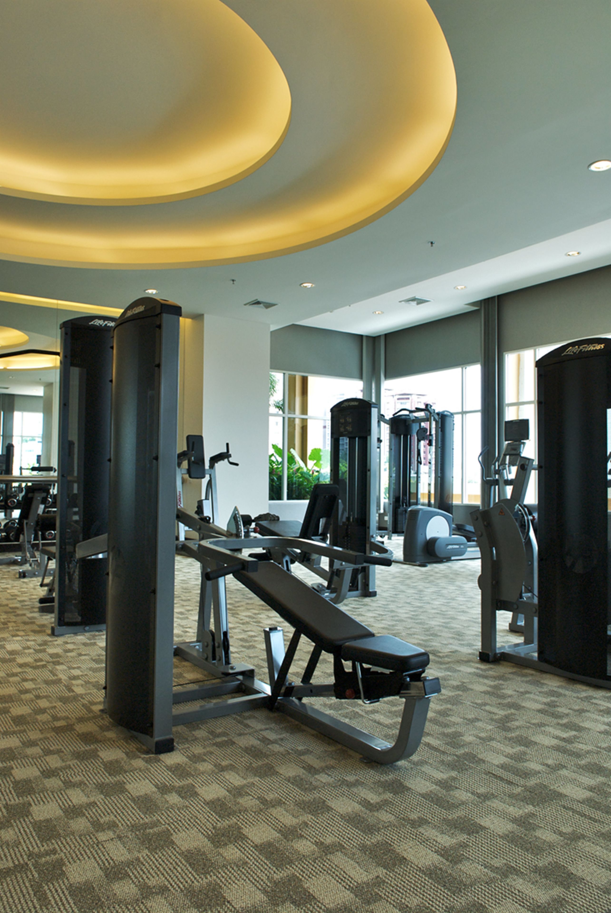Et fitnesscenter med forskellig træningsudstyr, store vinduer og gulvtæppe.