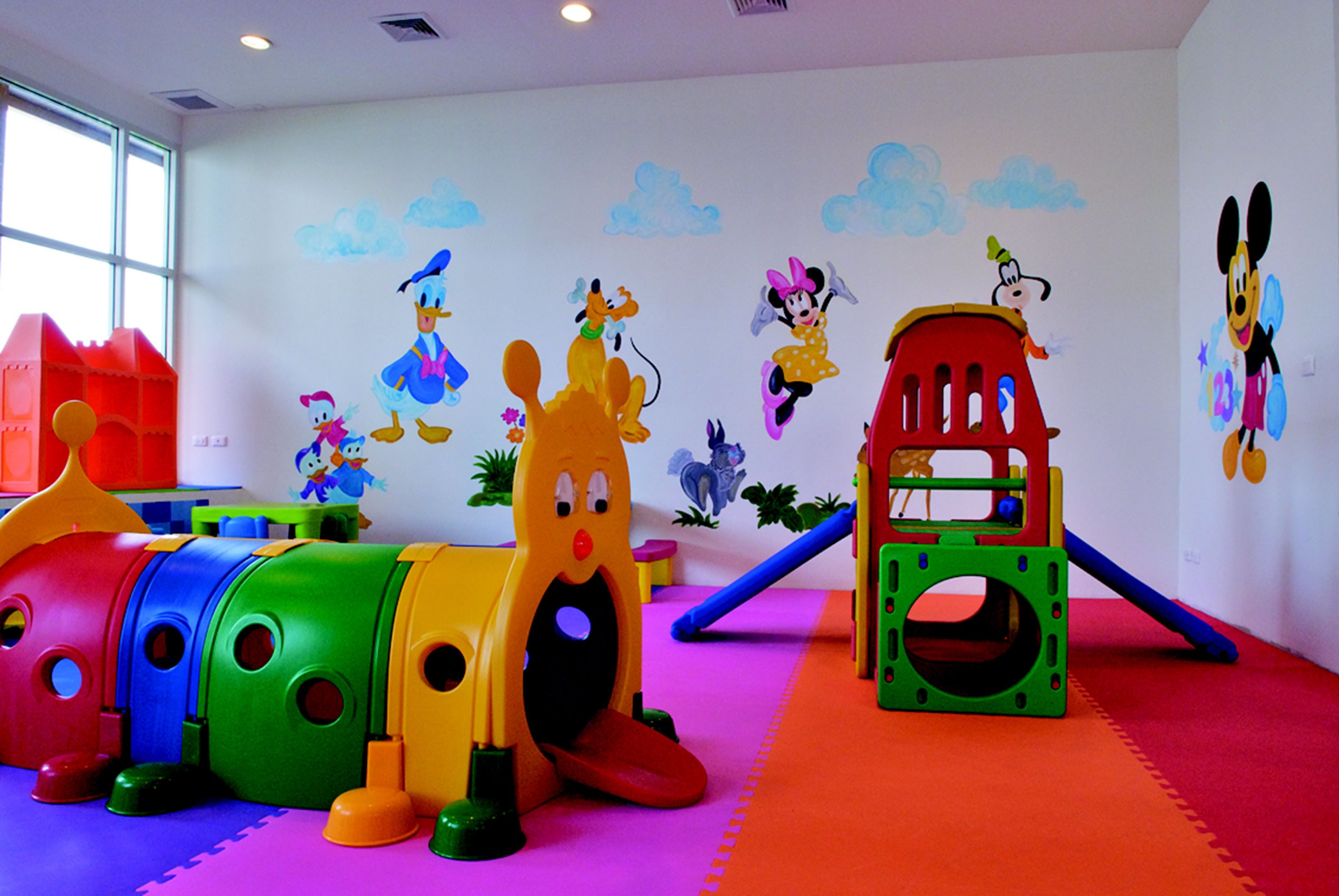 Ein Kinderspielbereich mit bunten Spielgeräten und Wandbildern mit Zeichentrickfiguren.