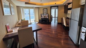 A modern hotel room with a dining area, a large window with curtains, a flat-screen TV, a refrigerator, and a ceiling light fixture. - (Bangkok)