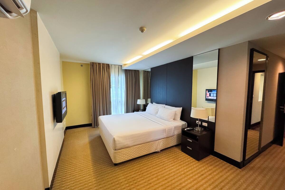 A hotel room with a large bed, bedside tables, a flat-screen TV, and a mirror.