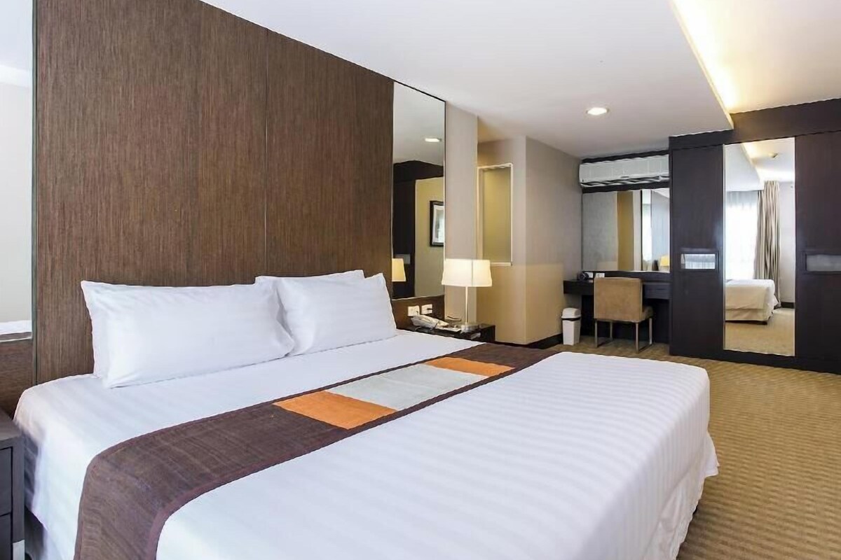 A hotel room with a large bed, a desk, a chair, a mirror, and a bathroom.