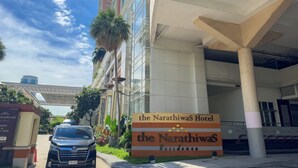The exterior of the Narathiwasa Hotel with a clear view of the building's facade, a parked SUV, and a signboard. - (Bangkok)
