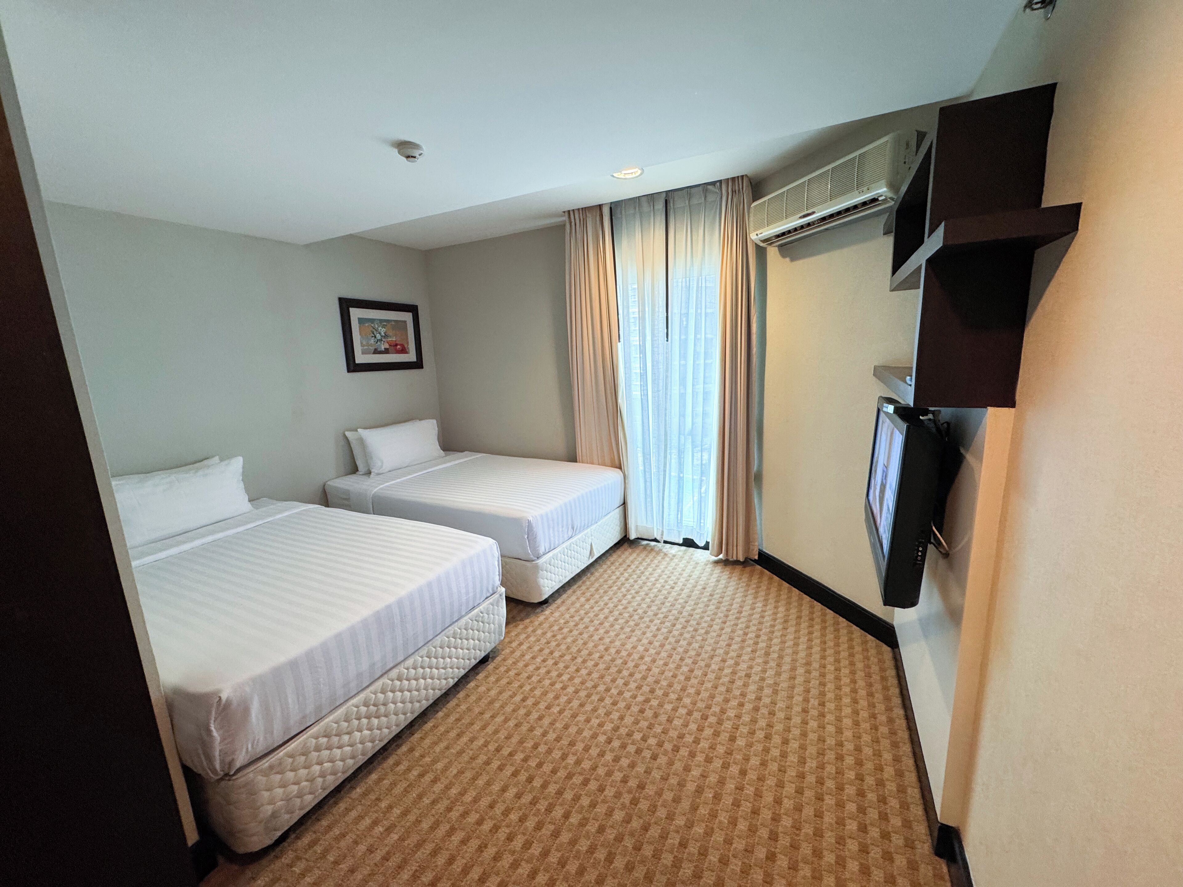 A hotel room with two beds, a flat-screen TV, an air conditioning unit, and a framed picture on the wall.