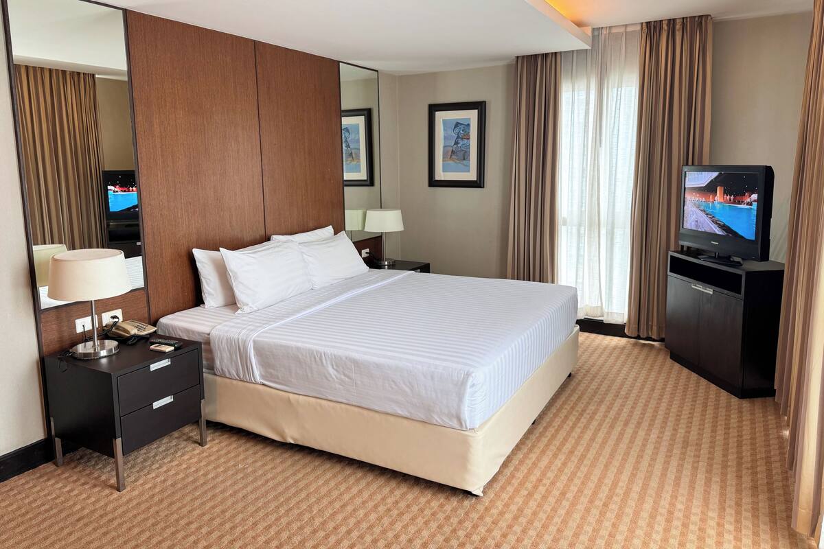 A hotel room with a large bed, a bedside table with a lamp, a TV, and a mirror.