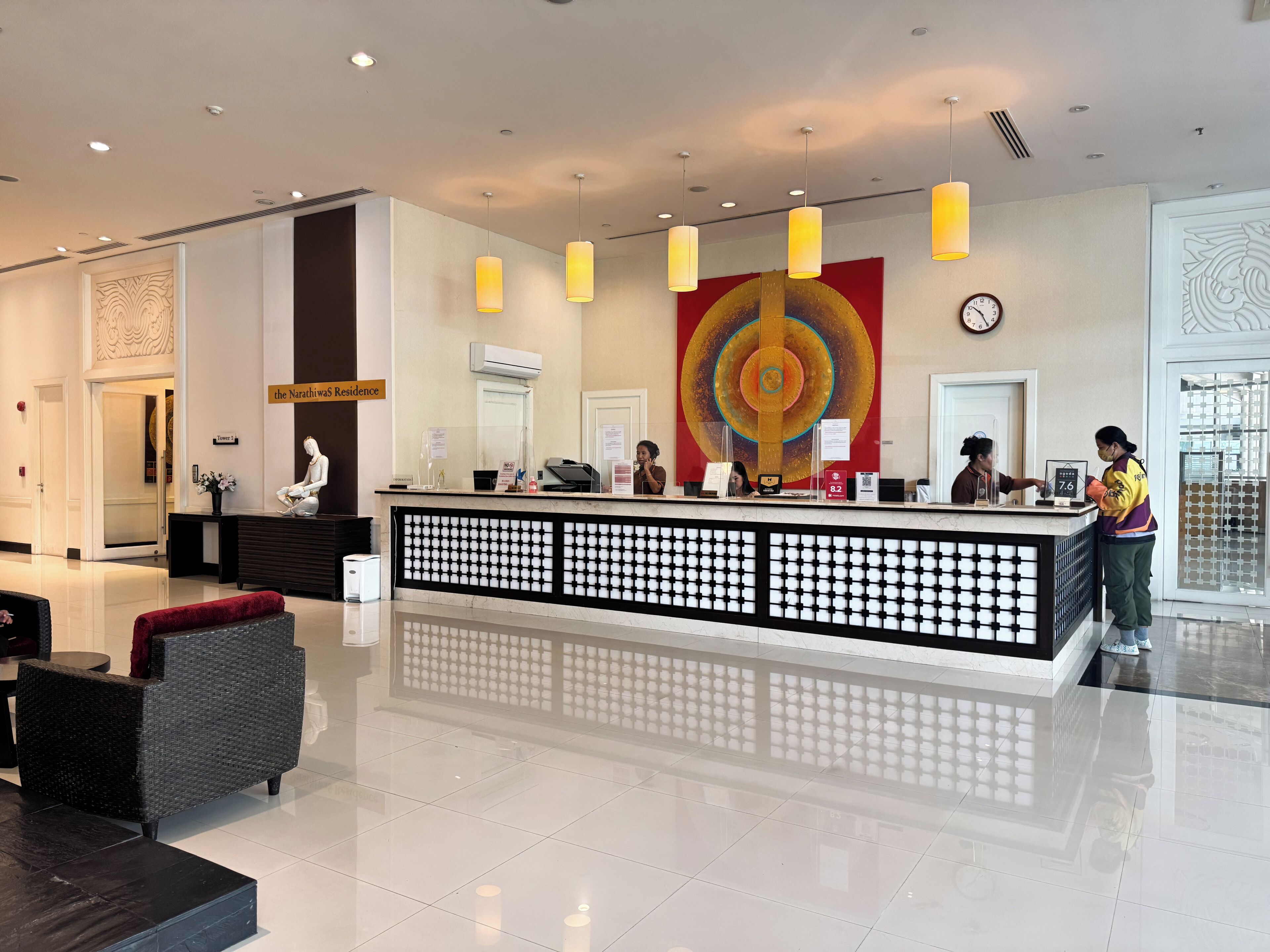 A hotel reception area with a modern design, including a reception desk, a large abstract artwork on the wall, and a clock.