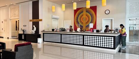 A hotel reception area with a modern design, including a reception desk, a large abstract artwork on the wall, and a clock.