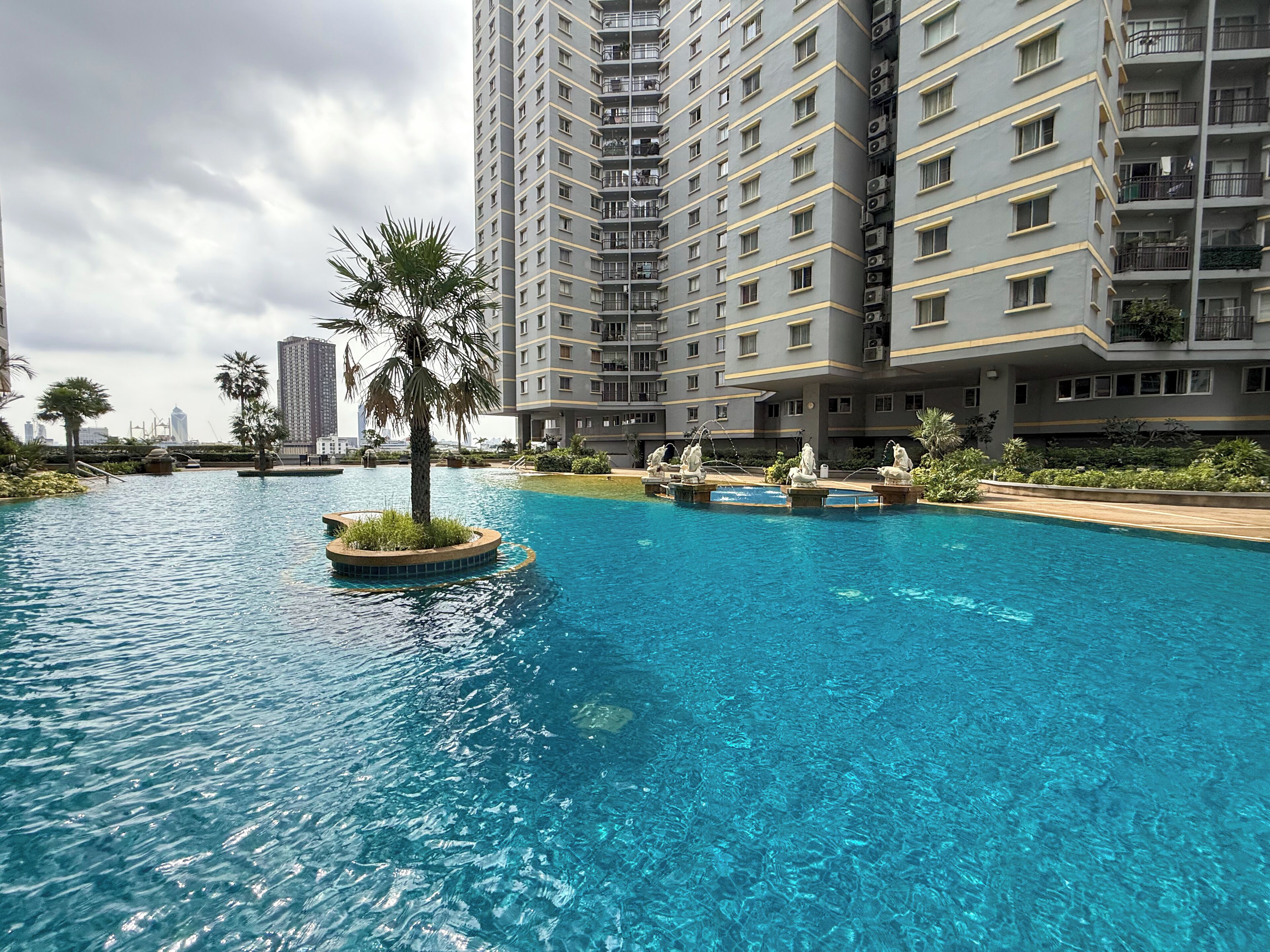 A swimming pool with a central island and surrounding statues, surrounded by high-rise residential buildings.