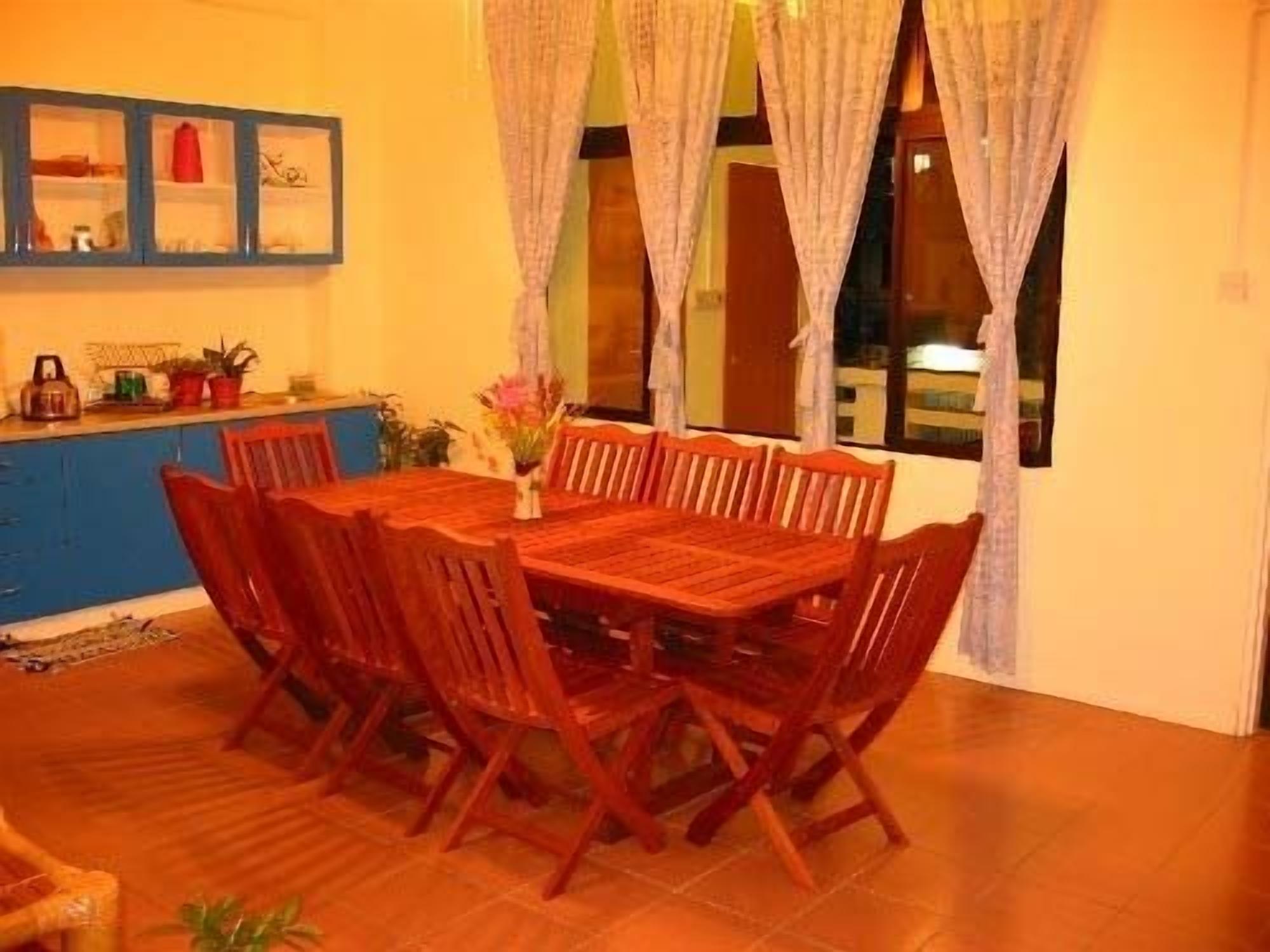 A dining area with a wooden table and chairs, a blue cabinet with glass doors, and a window with curtains.