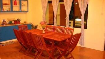 A dining area with a wooden table and chairs, a blue cabinet with glass doors, and a window with curtains.