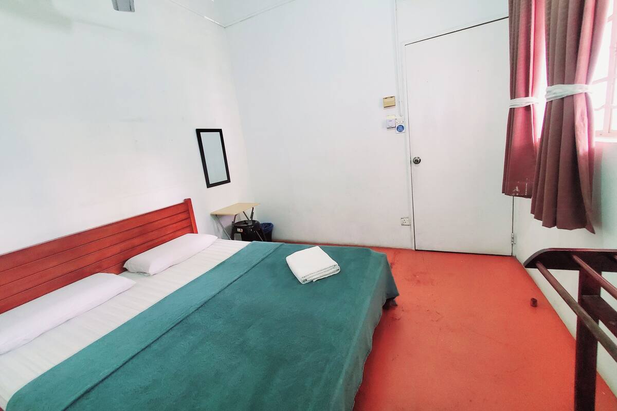 Hotellihuone, jossa on sänky, punainen matto, valkoinen ovi ja ikkuna, jossa on verhot.