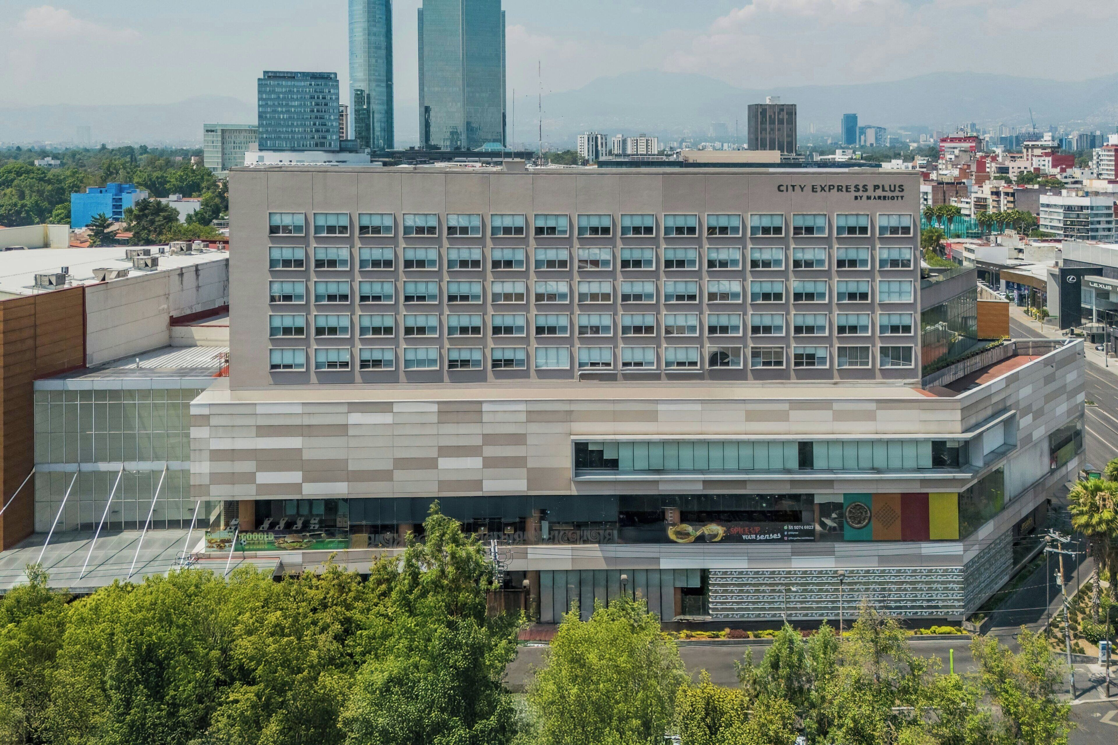 Een modern hotel met een raster van ramen, een plat dak en een bord met 'City Express Plus by Marriott'.