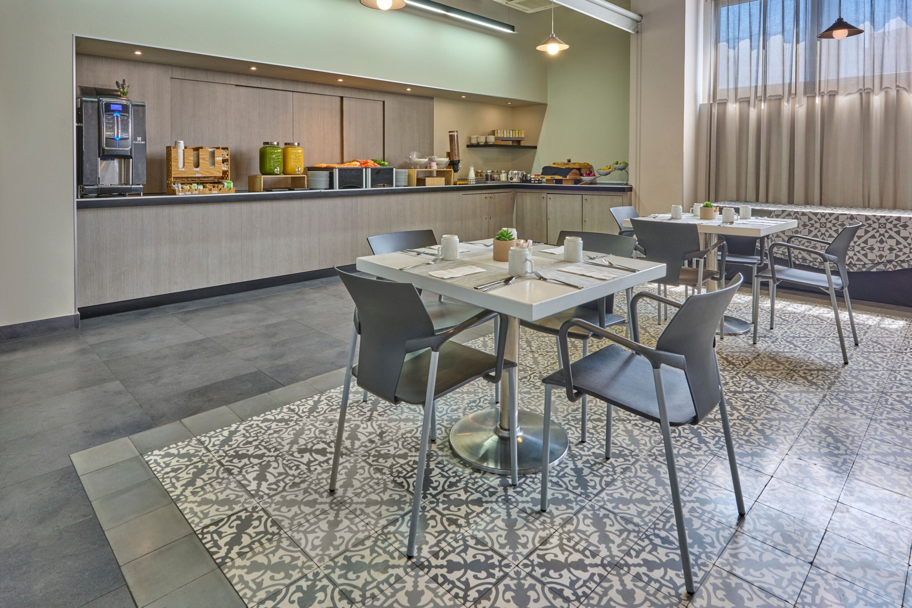 Een moderne keukenhoek met een ingebouwde koffieapparaat, een aanrecht met diverse etenswaren, en een zithoek met tafels en stoelen.