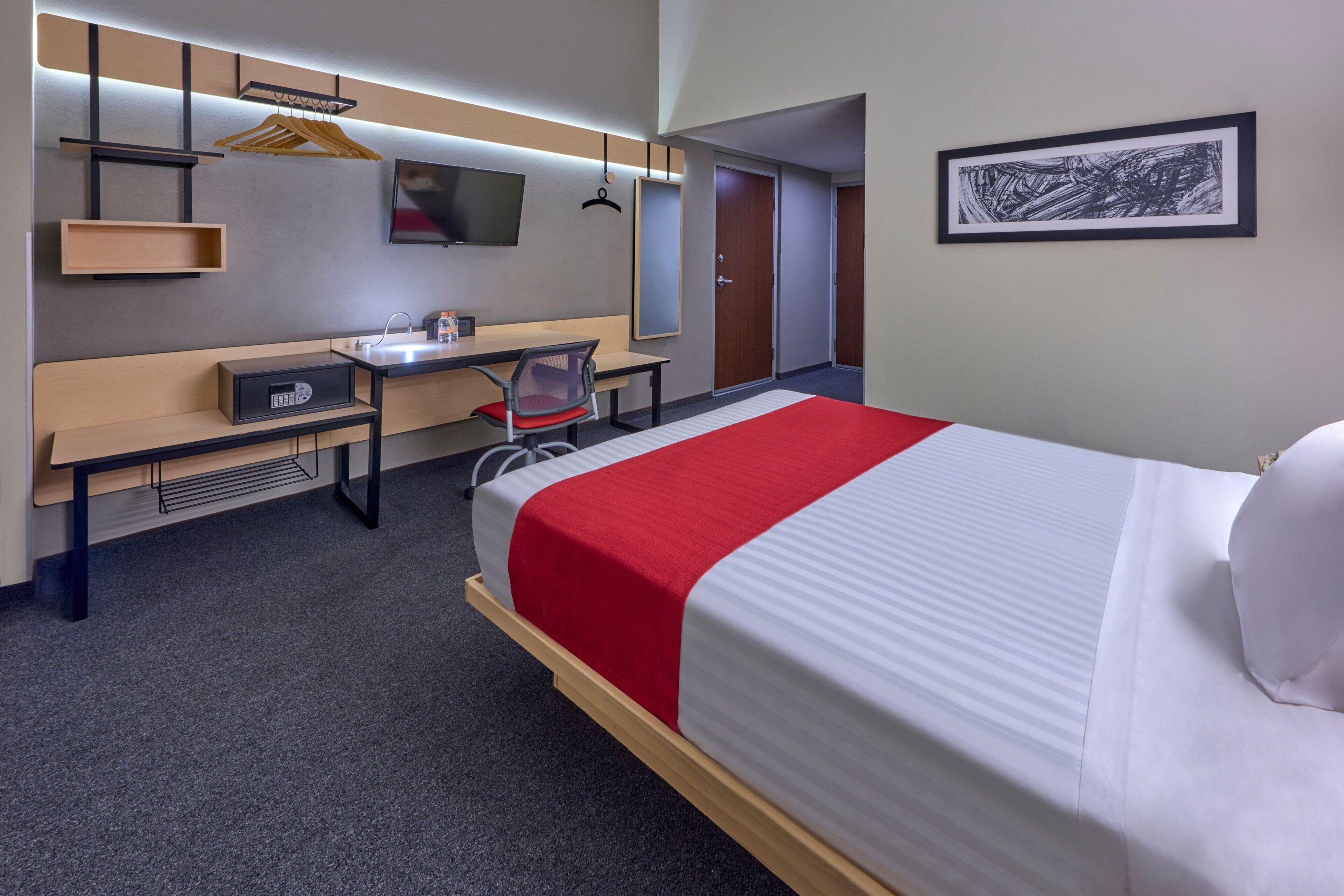 Ein Hotelzimmer mit Bett, Schreibtisch, Stuhl, Fernseher, Spiegel und Tür.