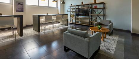 Un espace de bureau moderne avec un canapé gris, une table basse en bois et un téléviseur posé sur une étagère.