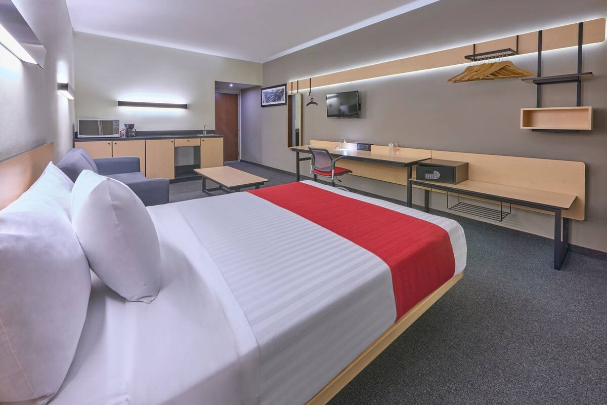 A hotel room with a bed, a desk, a chair, a TV, a microwave, and a small kitchenette.