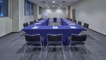 Un salón de conferencias con una larga mesa, sillas y una pantalla para proyector.