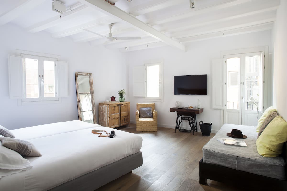 Quarto com cama, poltrona, televisão e escrivaninha.