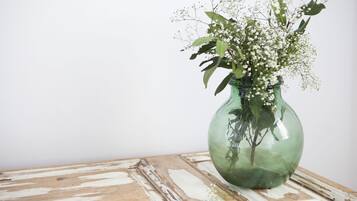 Un jarrón verde de vidrio con flores blancas y hojas verdes sobre una mesa de madera.