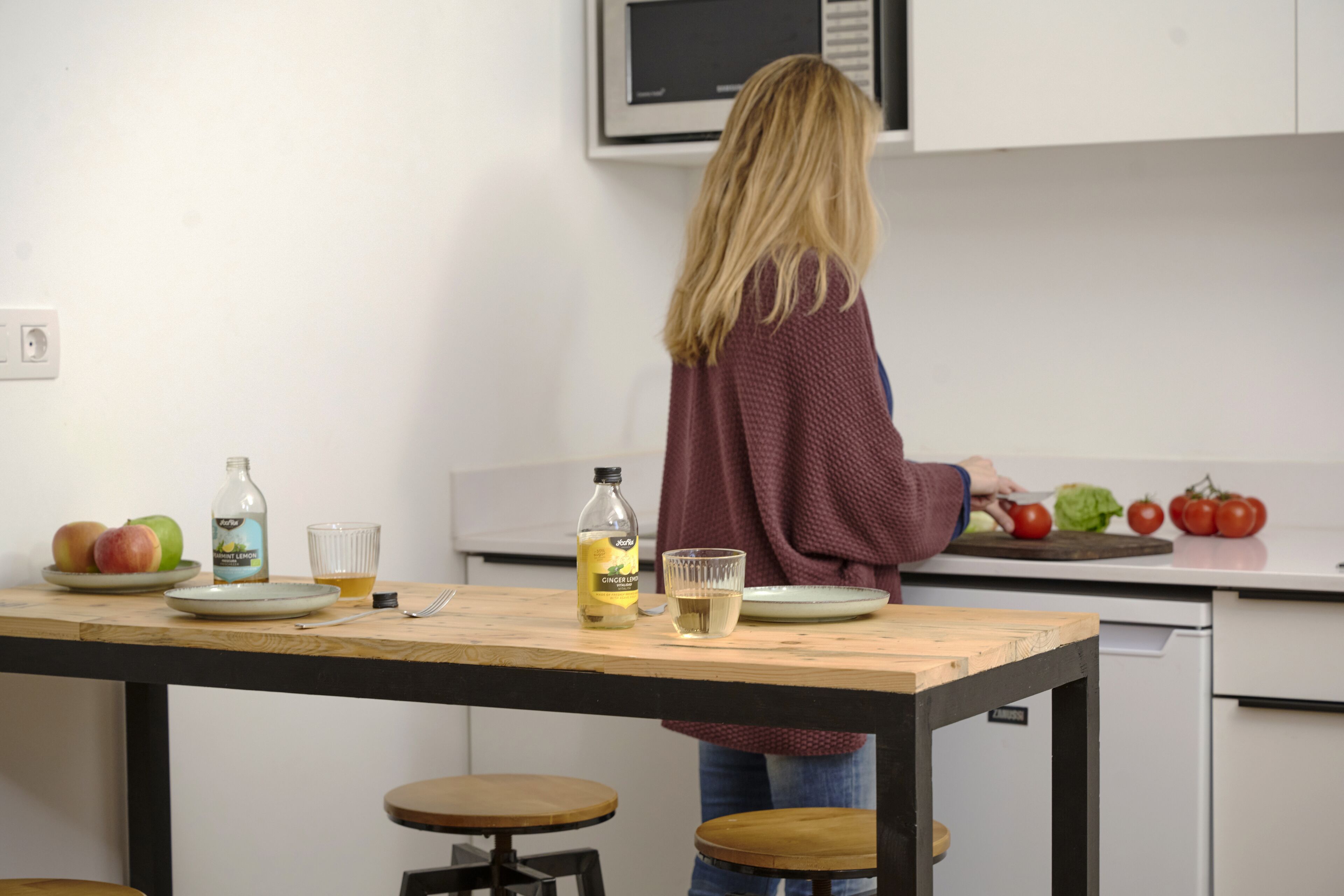 A kitchen with a table set for two, a microwave above the counter, and a person preparing food.