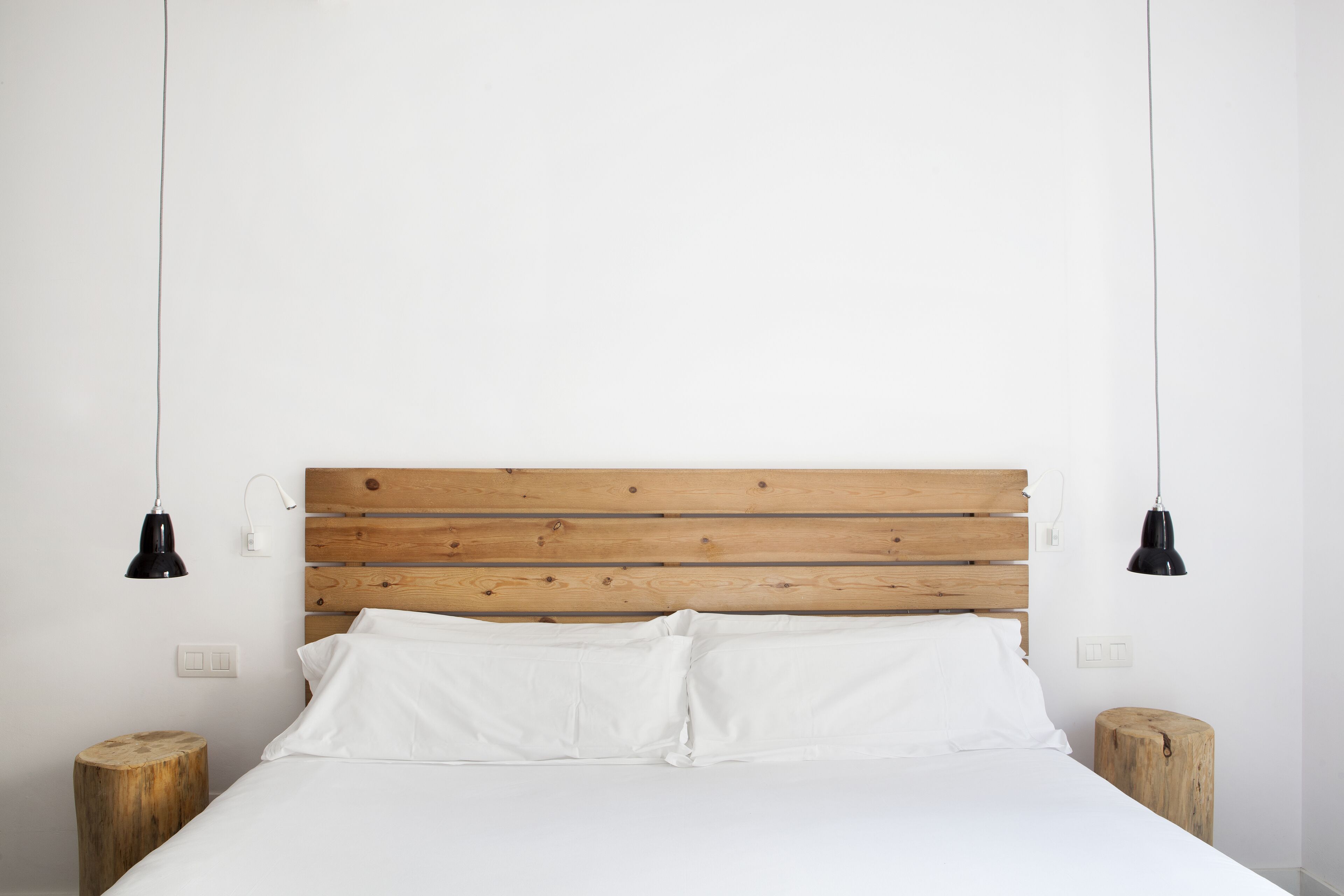A bed with white linens, a wooden headboard, and two bedside lamps.