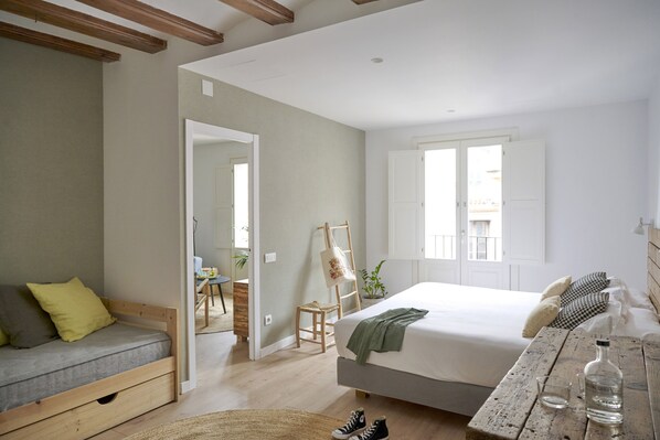 A bedroom with a bed, a wooden bench, a table with a bottle, and a ladder. - Eco Boutique Hostal Grau (Barcelona)