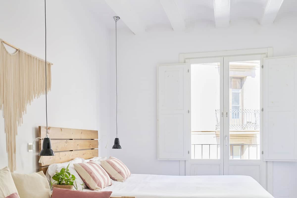 Quarto minimalista com uma cama de madeira, um sofá cinzento e uma decoração de macramé pendente na parede.
