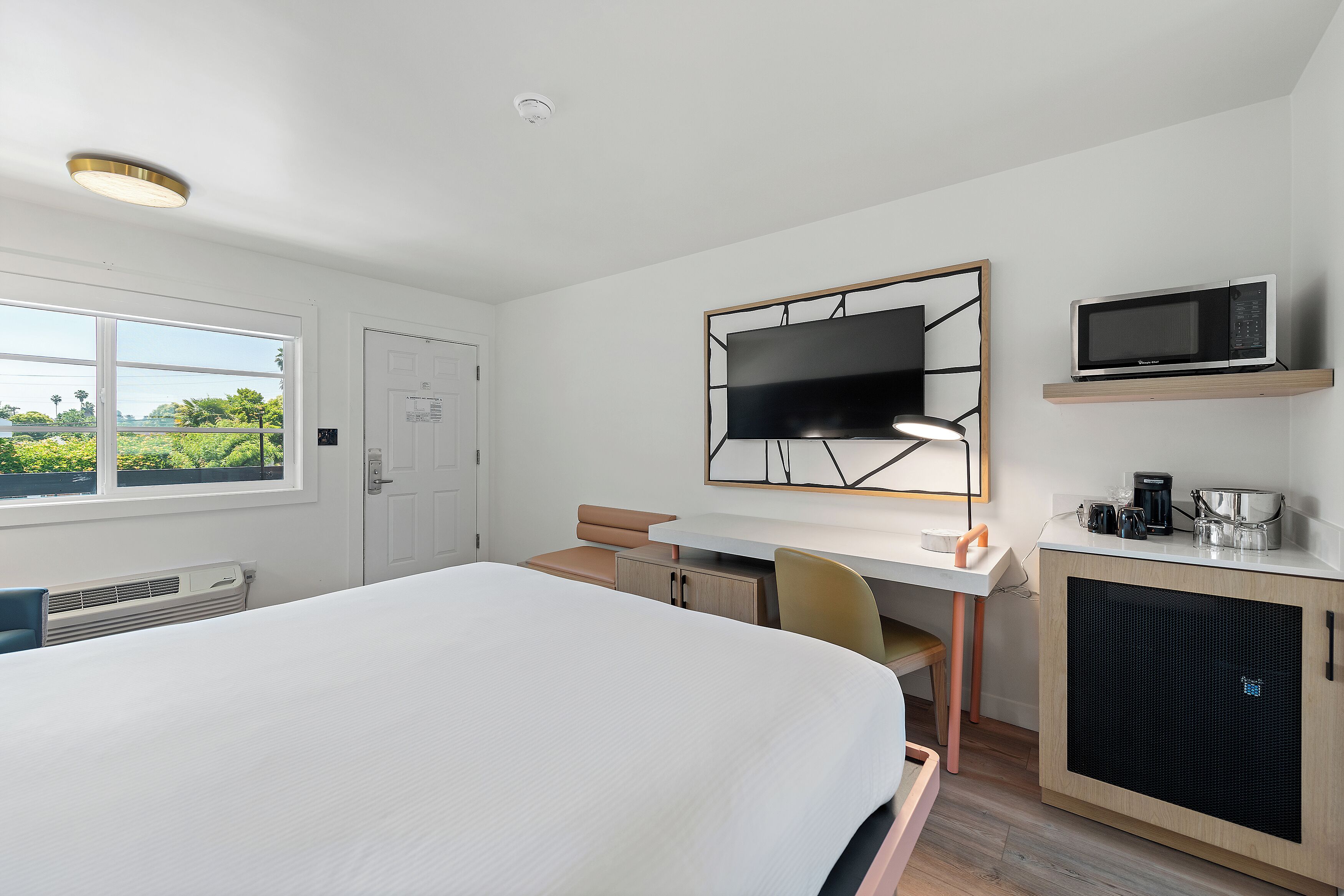 A hotel room with a large bed, a desk with a chair, a television, a microwave, and a small kitchenette.