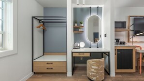 A compact bedroom with a bed, a desk with a mirror, shelves with plants, and a TV. -  GoodSpring Motel (Napa)