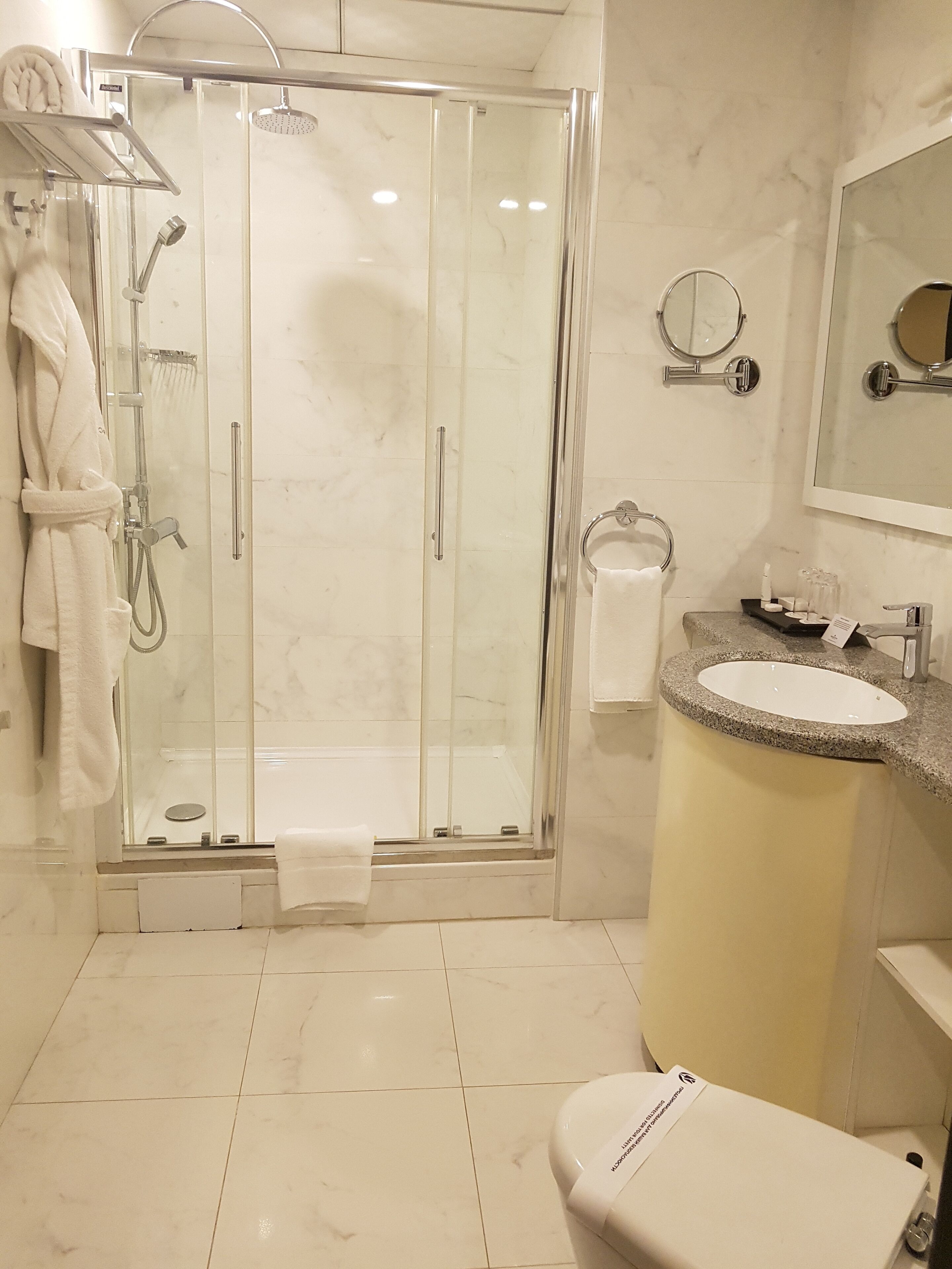 Un baño moderno con ducha envuelta en vidrio, lavamanos de granito, inodoro y espejo.