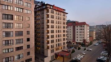 A multi-story hotel with a prominent "RAMADA" sign, featuring a modern architectural design with balconies and a parking area in front.