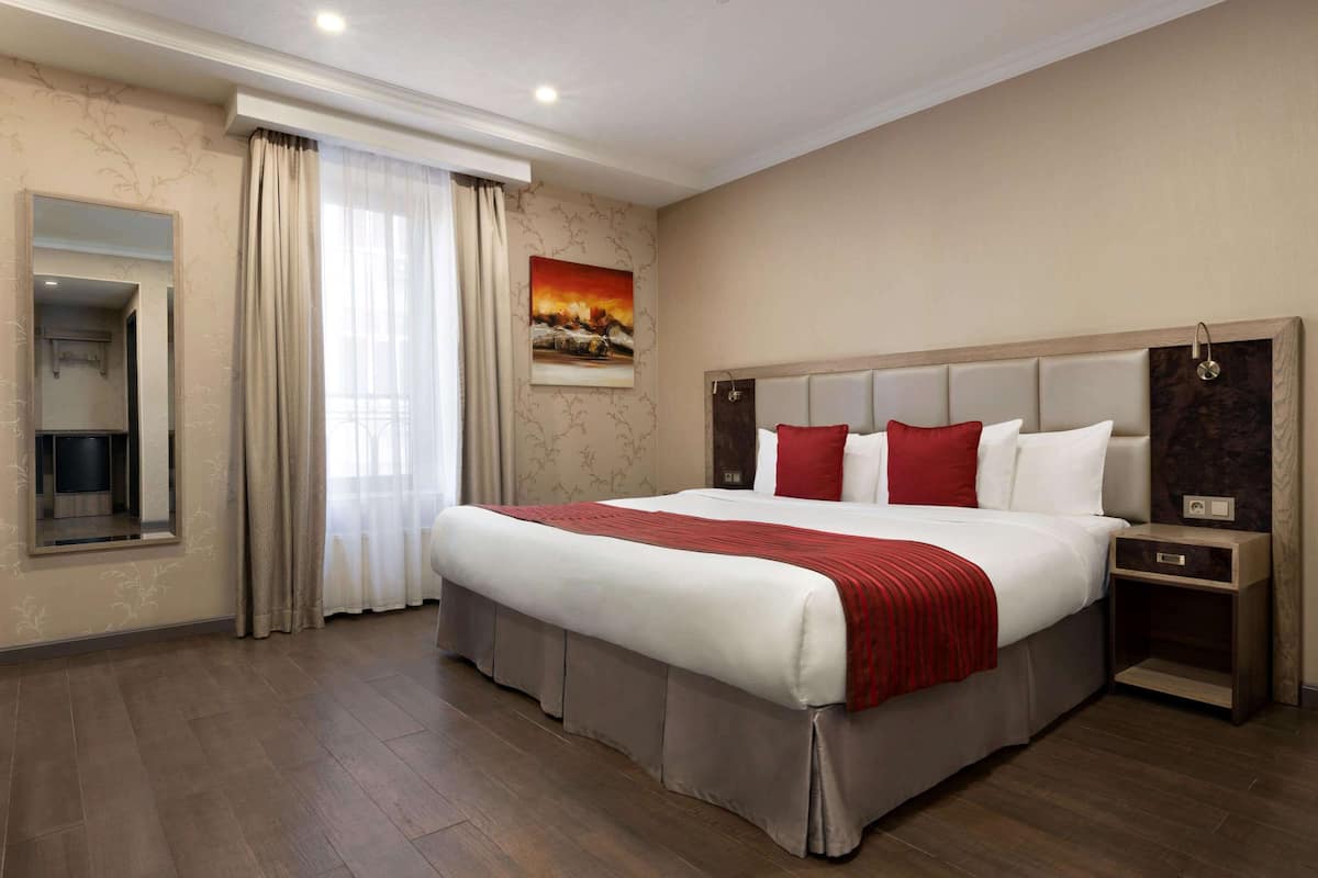 Amplia habitación de hotel con una cama grande, una mesita de noche, un espejo y un cuadro en la pared.