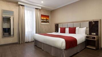 Quarto de hotel espaçoso com uma cama grande, mesa de cabeceira, espelho e um quadro na parede.